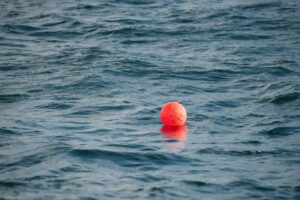 A vibrant red buoy gently floats on the calm ocean, reflecting sunlight.